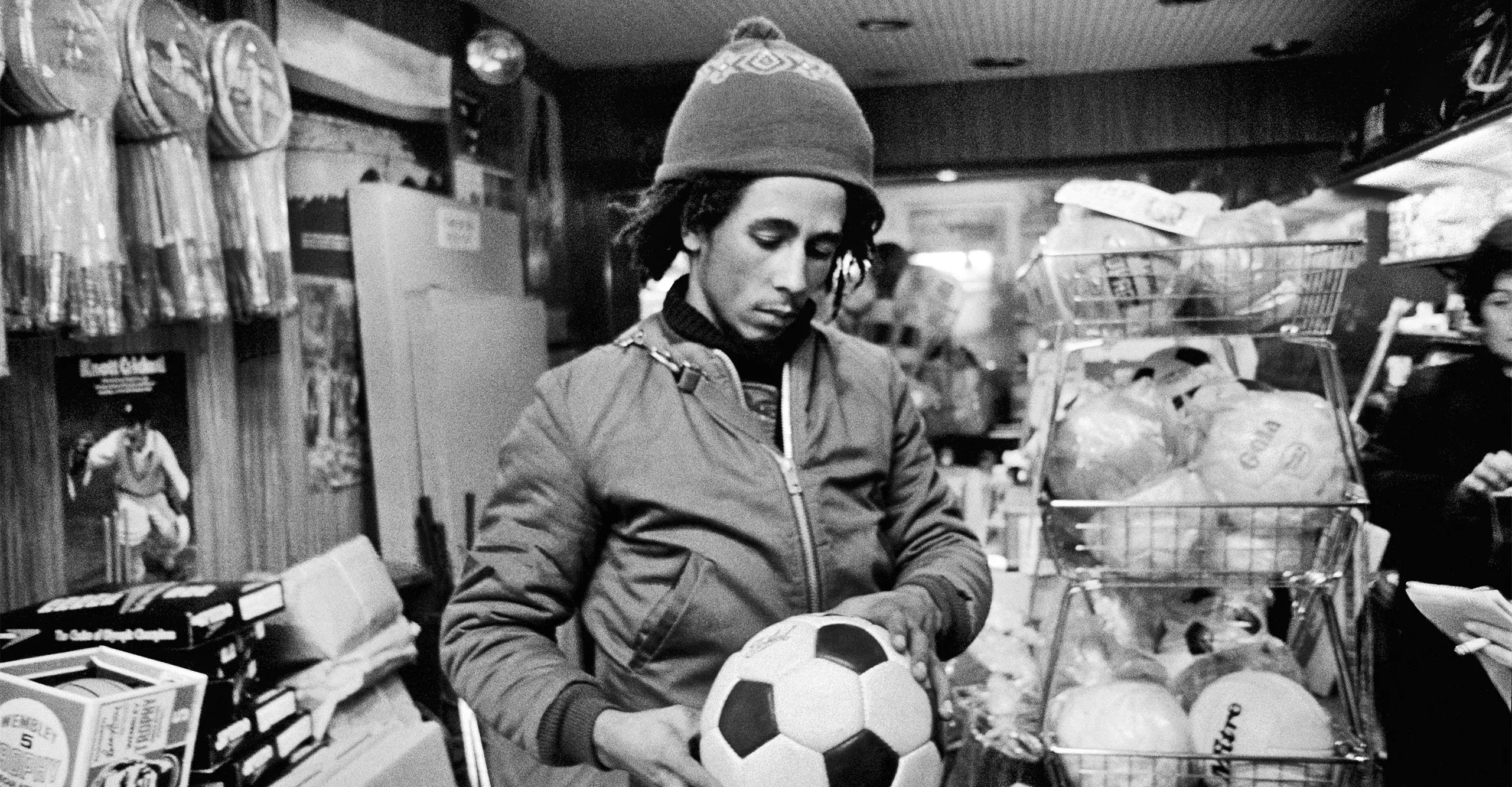 Black and white photo of Bob Marley in a shop holding a football